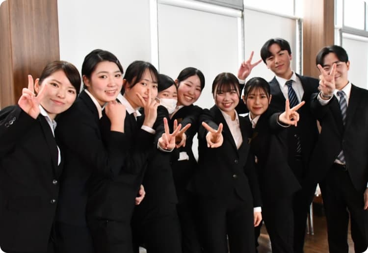 スーツを着た男女9人学生たちがこちらにピースしている様子