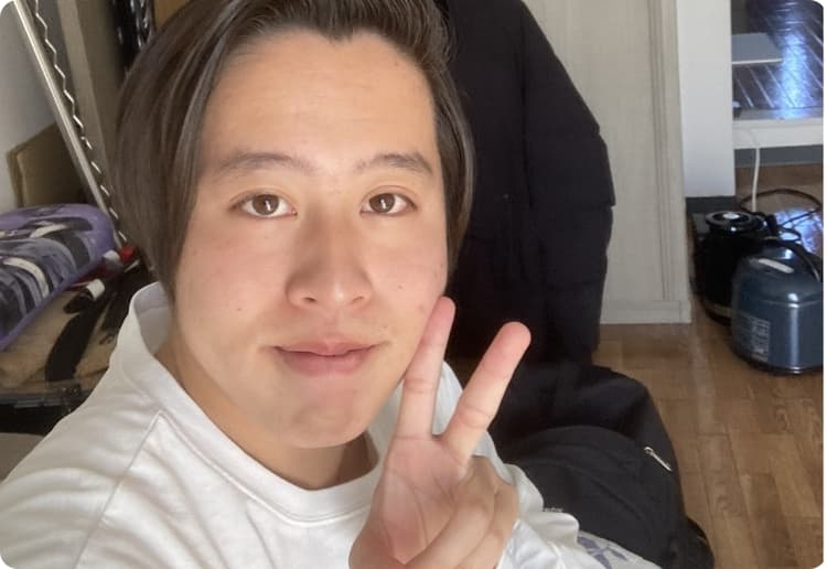男子学生が1人暮らしの部屋でピースしている様子